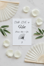 Our Love is Hot sign flat lay with open ivory hand fans and eucalyptus